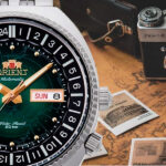 Reloj Orient World Map Revival Green RA-AA0E02E19B en mesa con cámara de fotos y sobre mapa del mundo